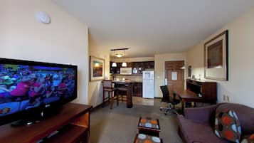 Una sala de estar con una televisión de pantalla plana, un sofá, una mesa de centro y una cocina al fondo.