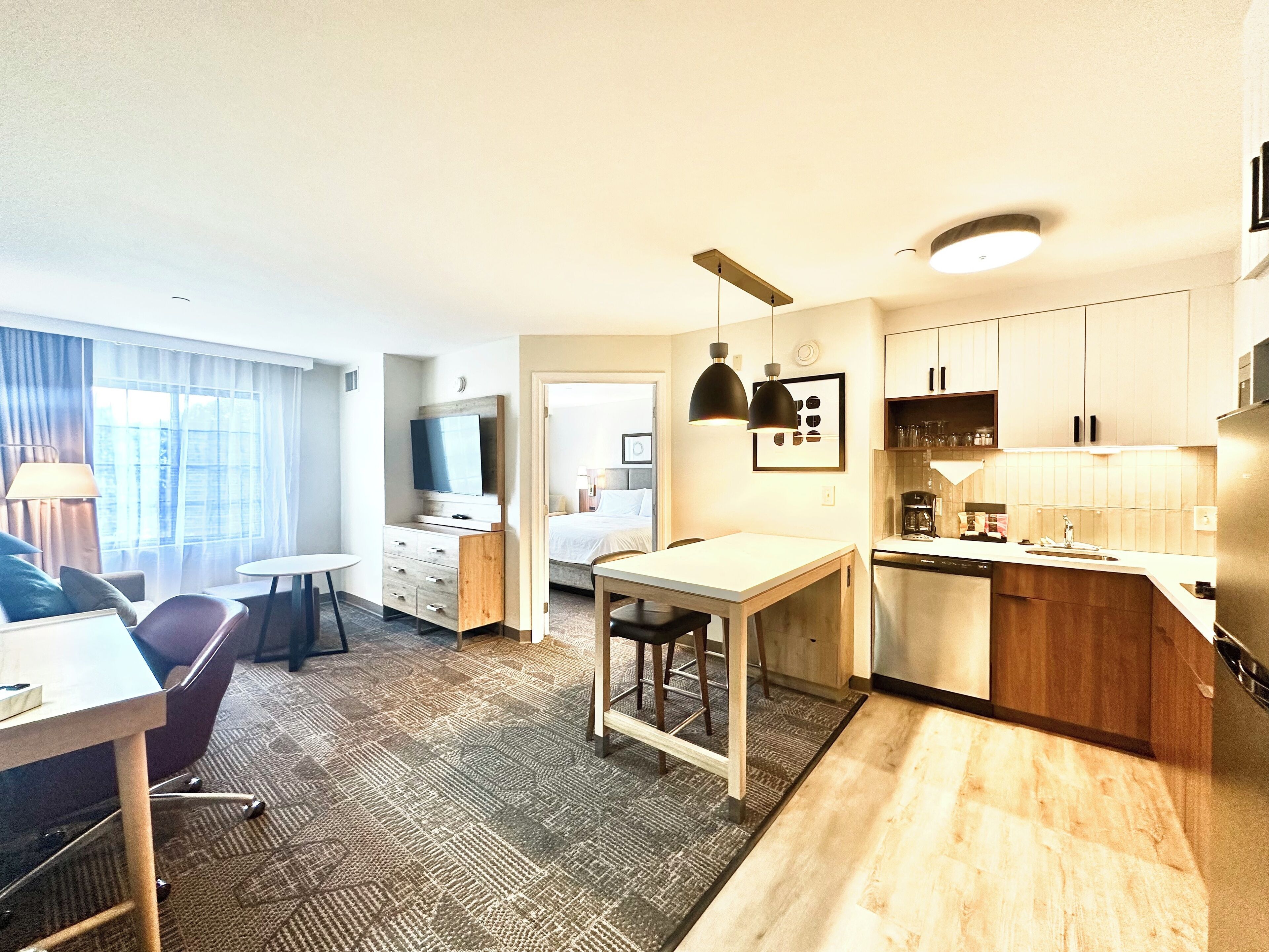 A modern hotel room with a dining area, kitchenette, and a bed.