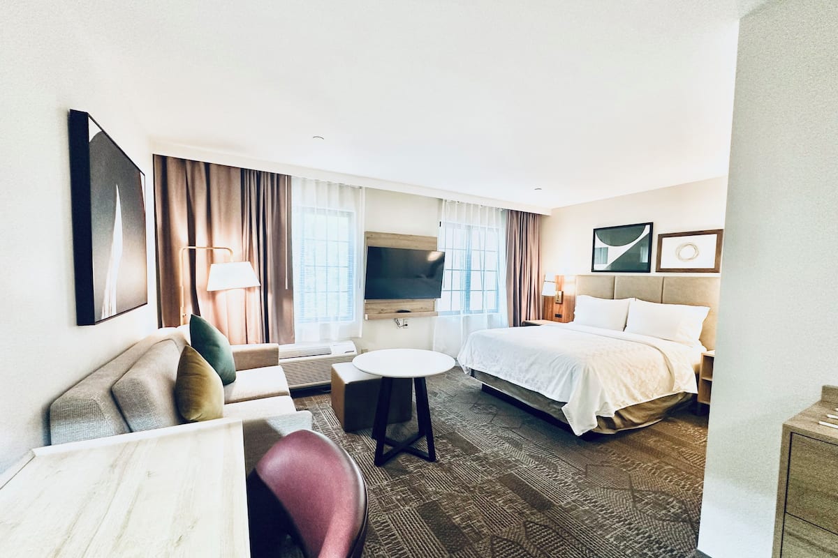 A hotel room with a bed, a desk, a chair, a TV, and a window with curtains.
