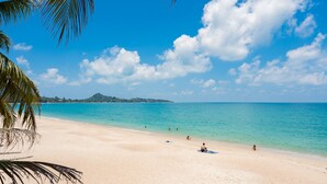 Une plage à l’eau turquoise et limpide, bordée d’un rivage sablonneux et de palmiers.