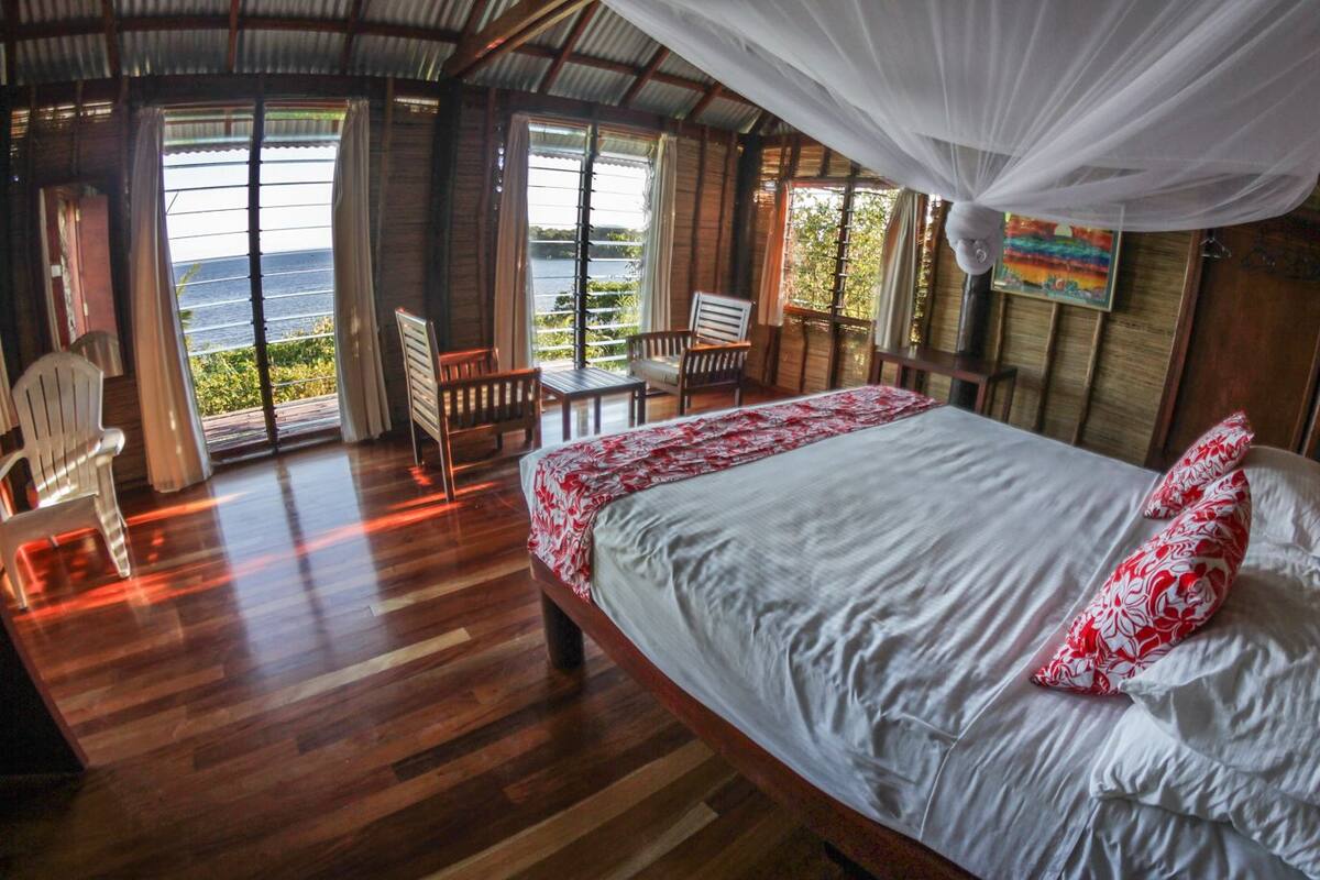 A room with a bed, a chair, and a view of the sea.