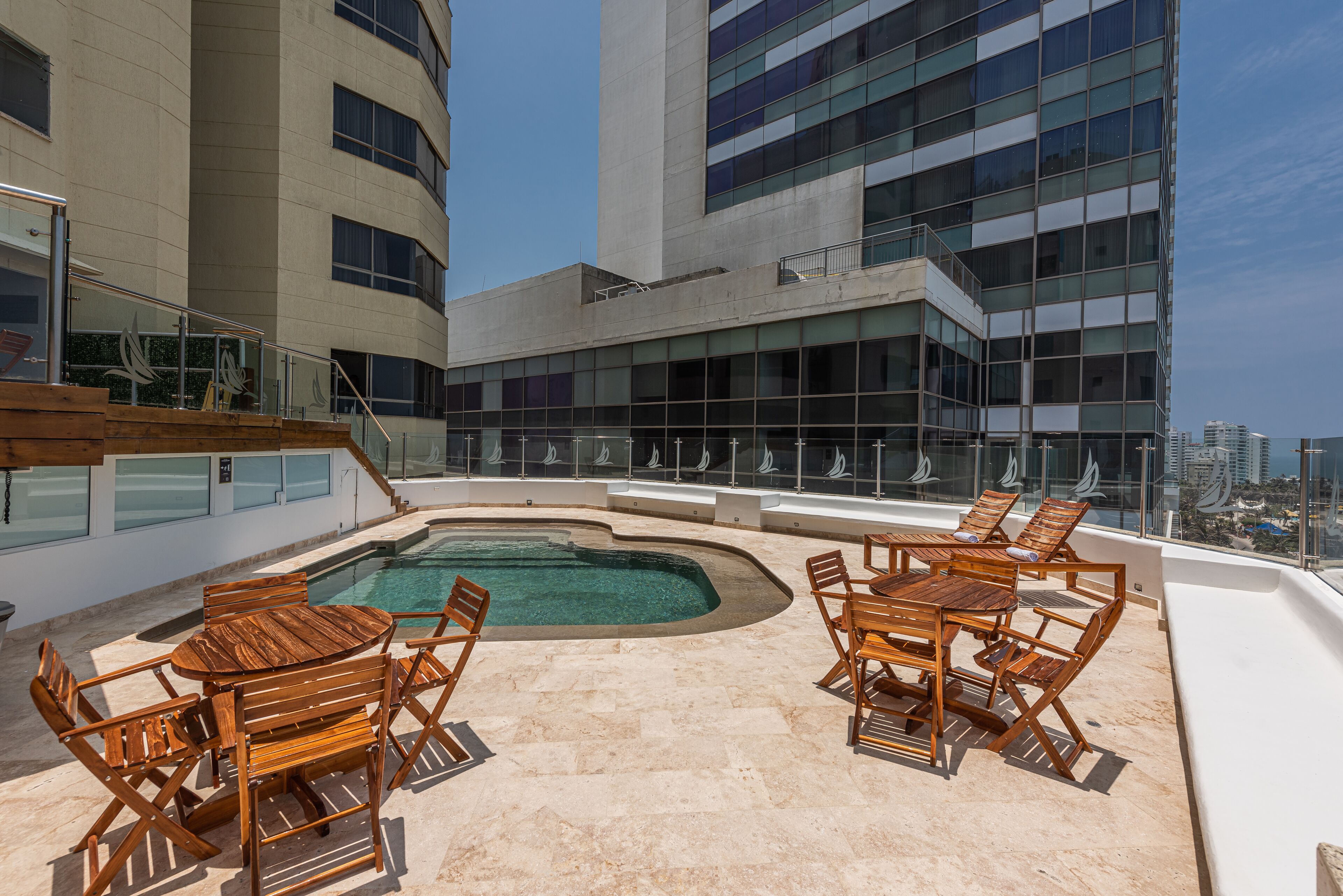 A rooftop pool area with wooden furniture and a view of a cityscape.