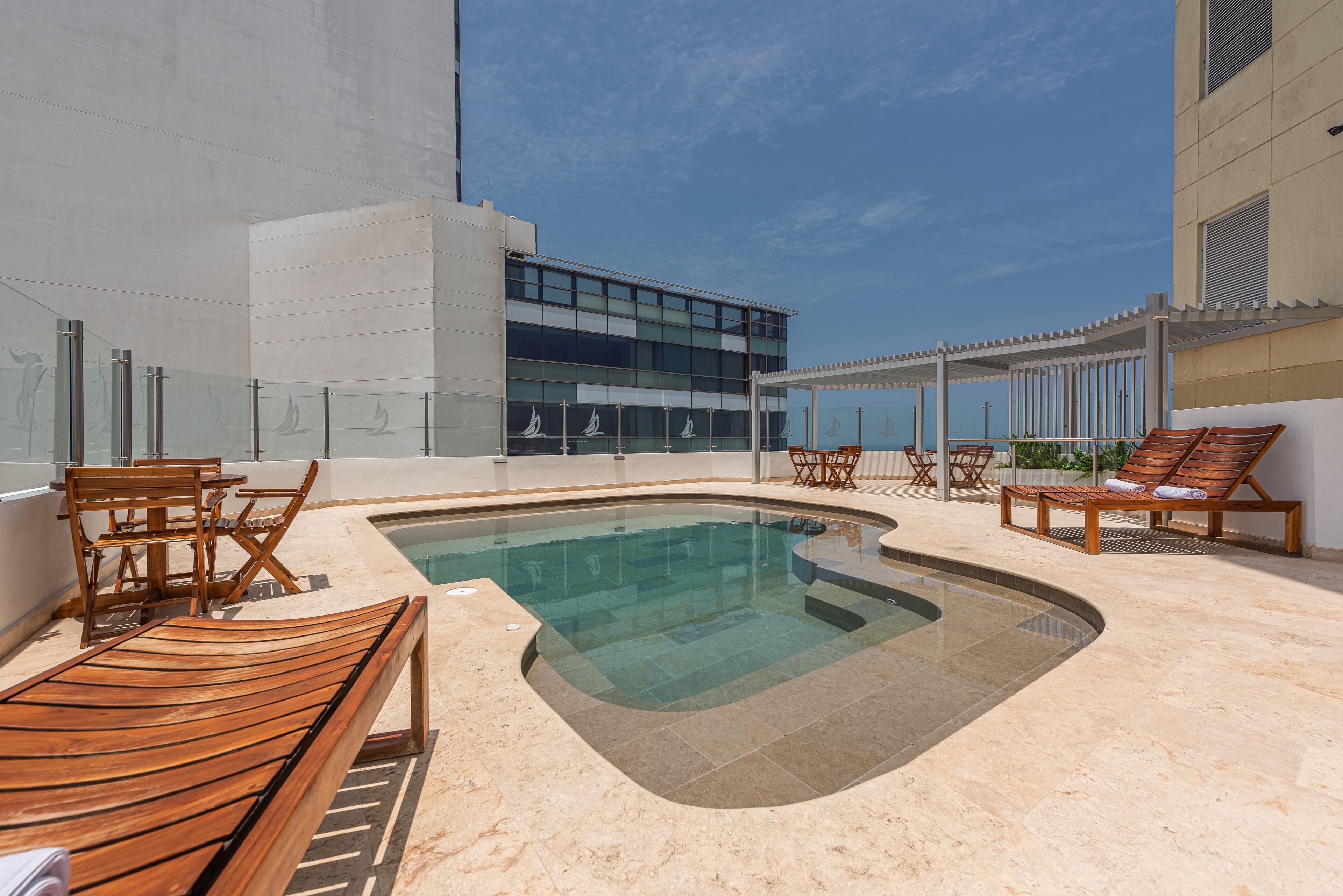 A modern pool area with a glass-enclosed pool, wooden loungers, and a glass railing.