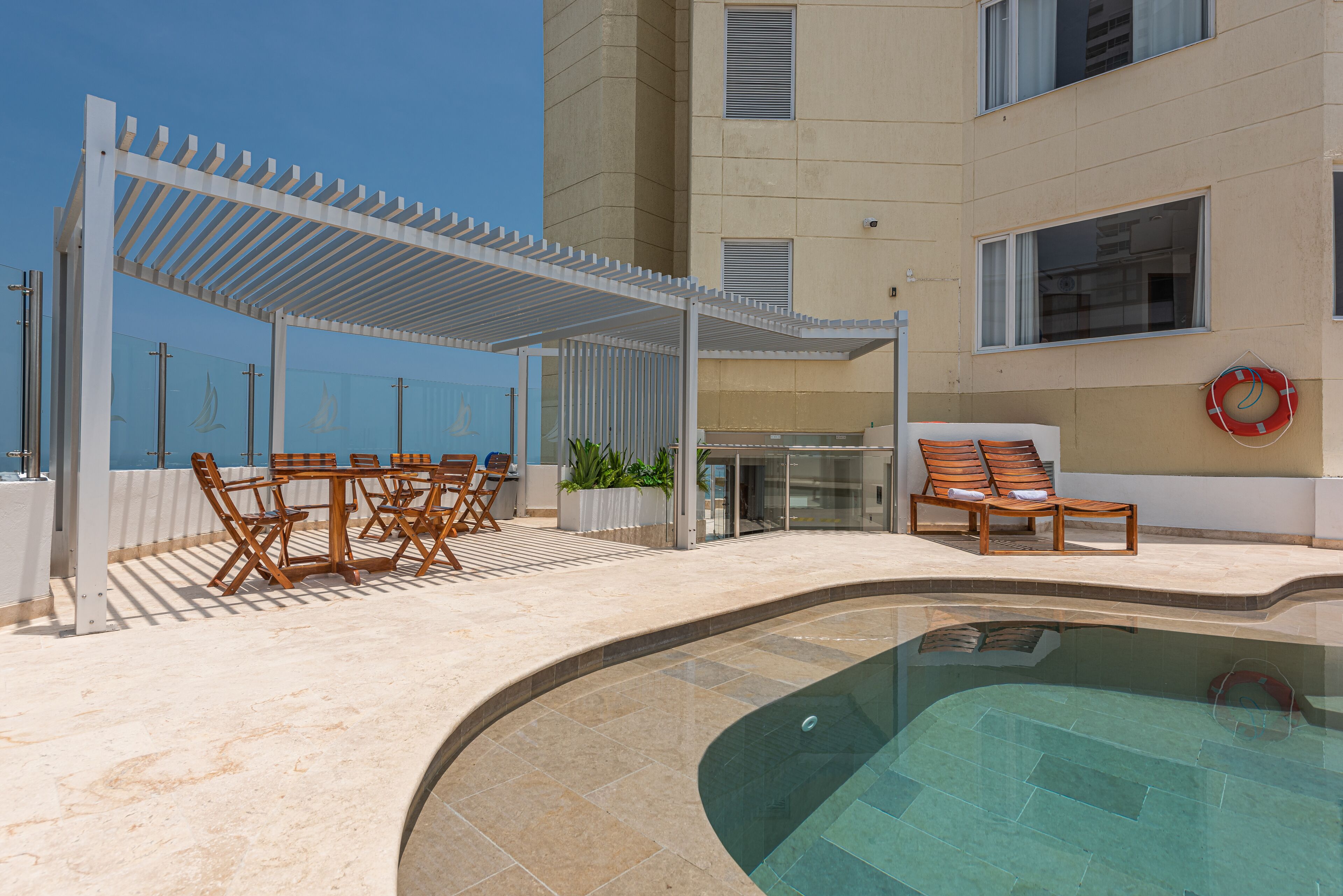 Un espace piscine agrémenté d’une pergola, de chaises longues et d’un bâtiment entièrement vitré.