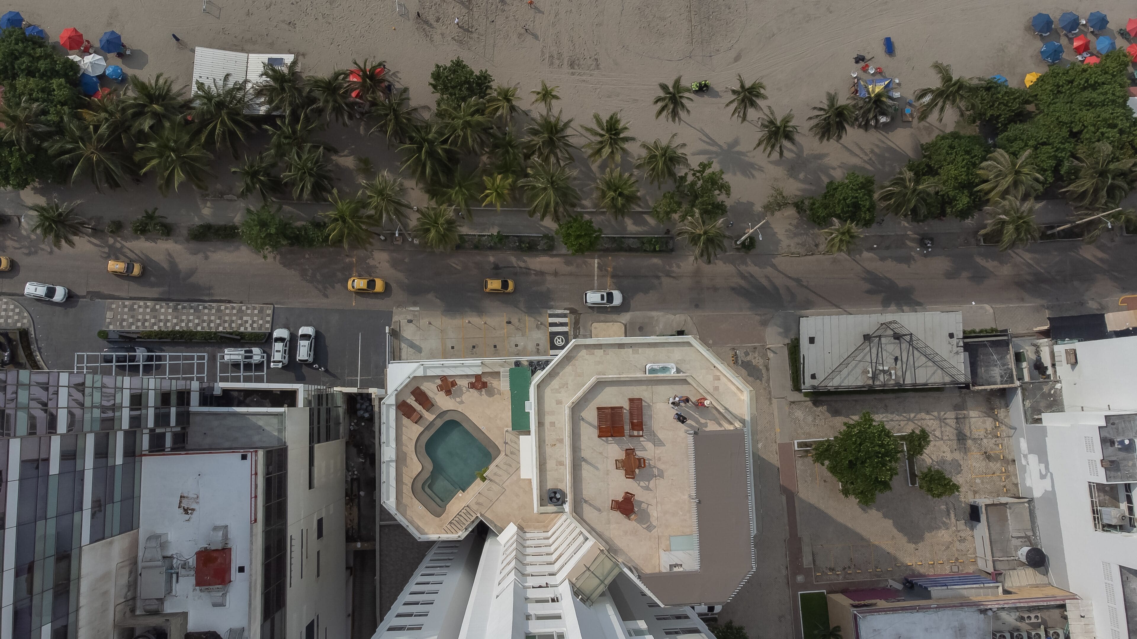 An aerial view of a resort with a swimming pool, outdoor seating, and palm trees.