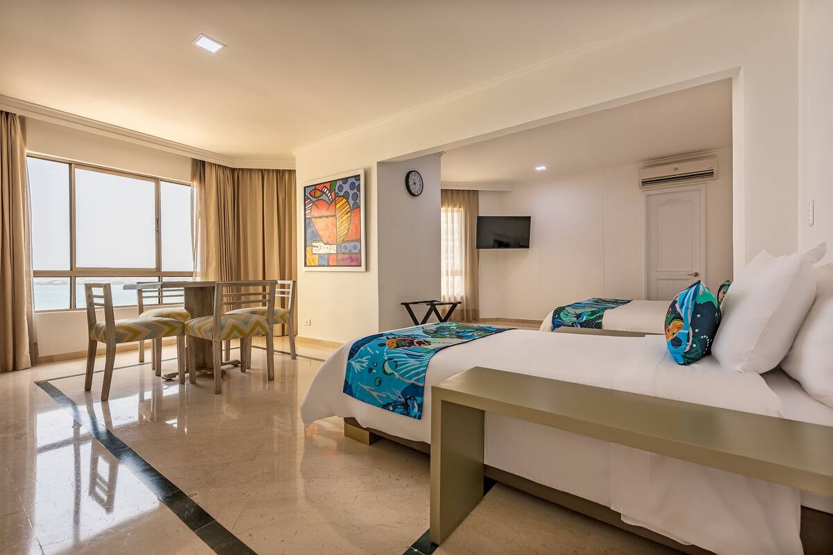 A hotel room with a bed, a desk, a chair, a TV, and a window with curtains.