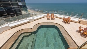 Una piscina en la azotea con agua cristalina, rodeada de sillones de descanso y vistas al océano.