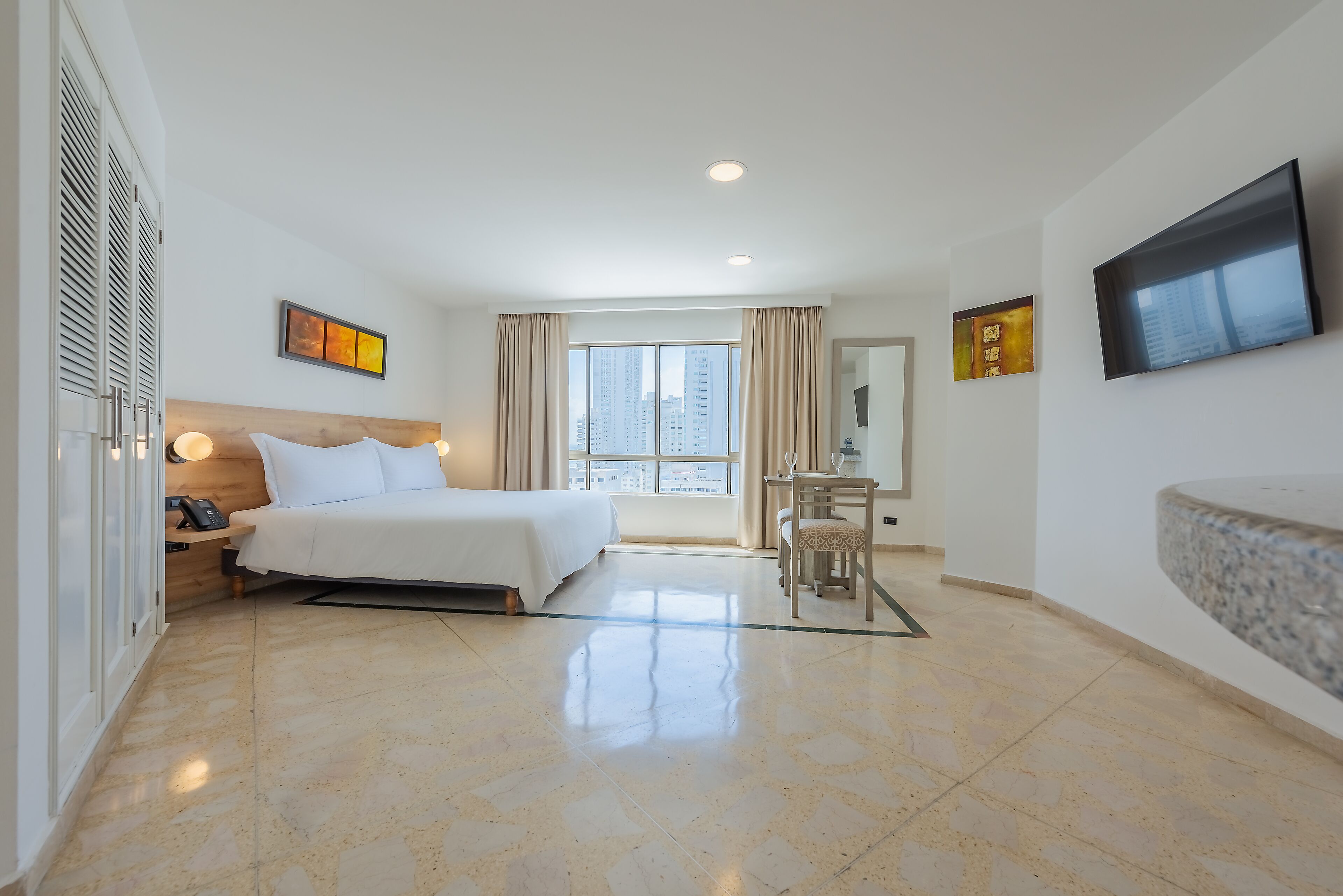 Una habitación de hotel con cama, mesita de noche, lámpara y televisor en la pared.
