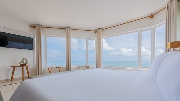 Una cama grande en una habitación de hotel con vistas al mar a través de amplios ventanales.