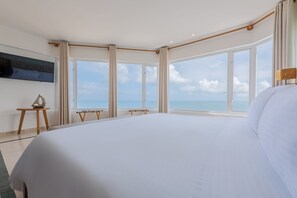 Un grand lit dans une chambre d’hôtel avec vue sur la mer, grâce à de grandes fenêtres.