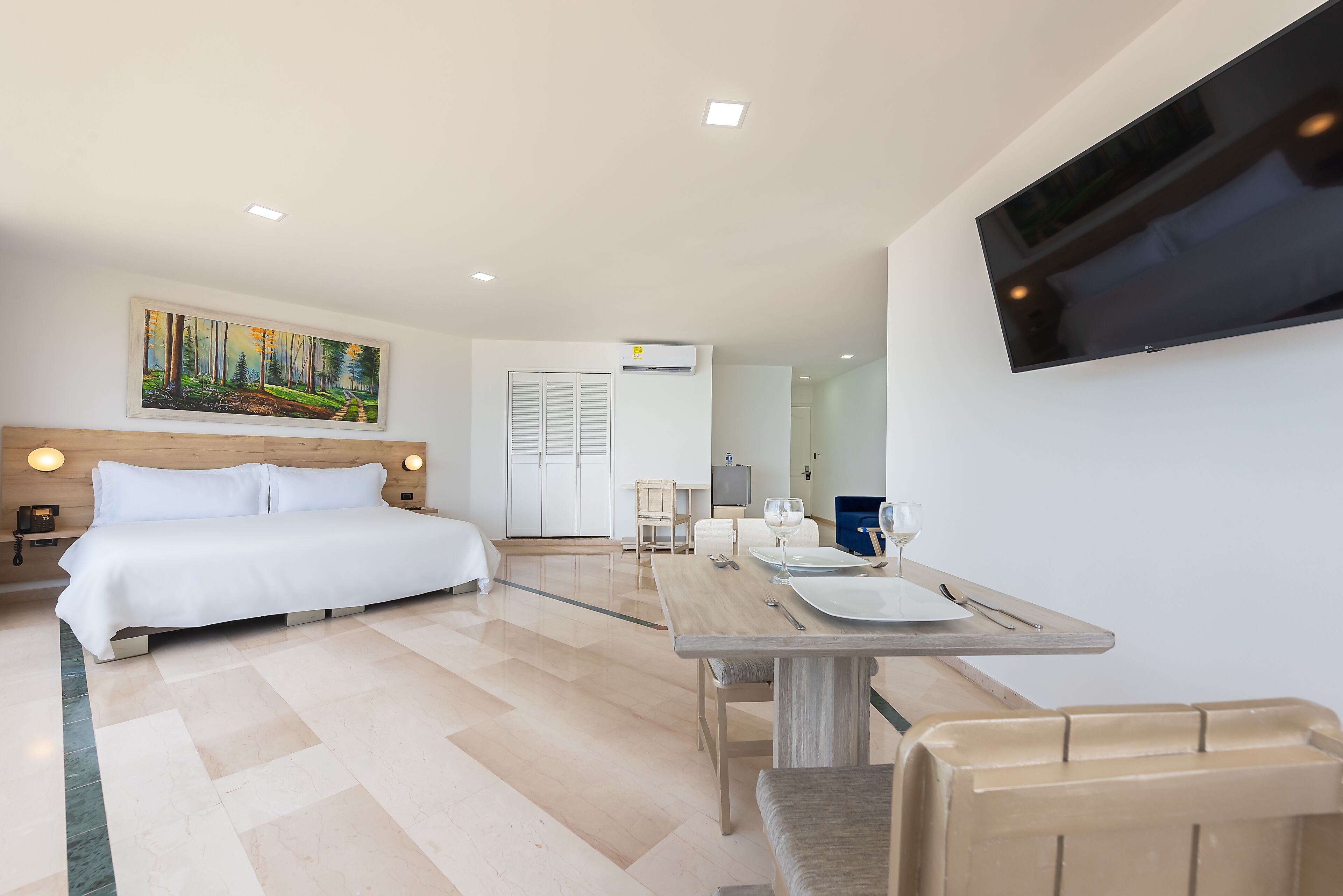 Une chambre d’hôtel comprenant un lit, un tableau, une télévision, une table à manger avec des chaises et un appareil de climatisation.