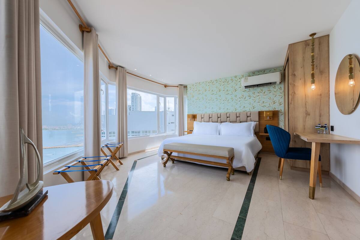 A hotel room with a large bed, a desk, and a view of the sea.