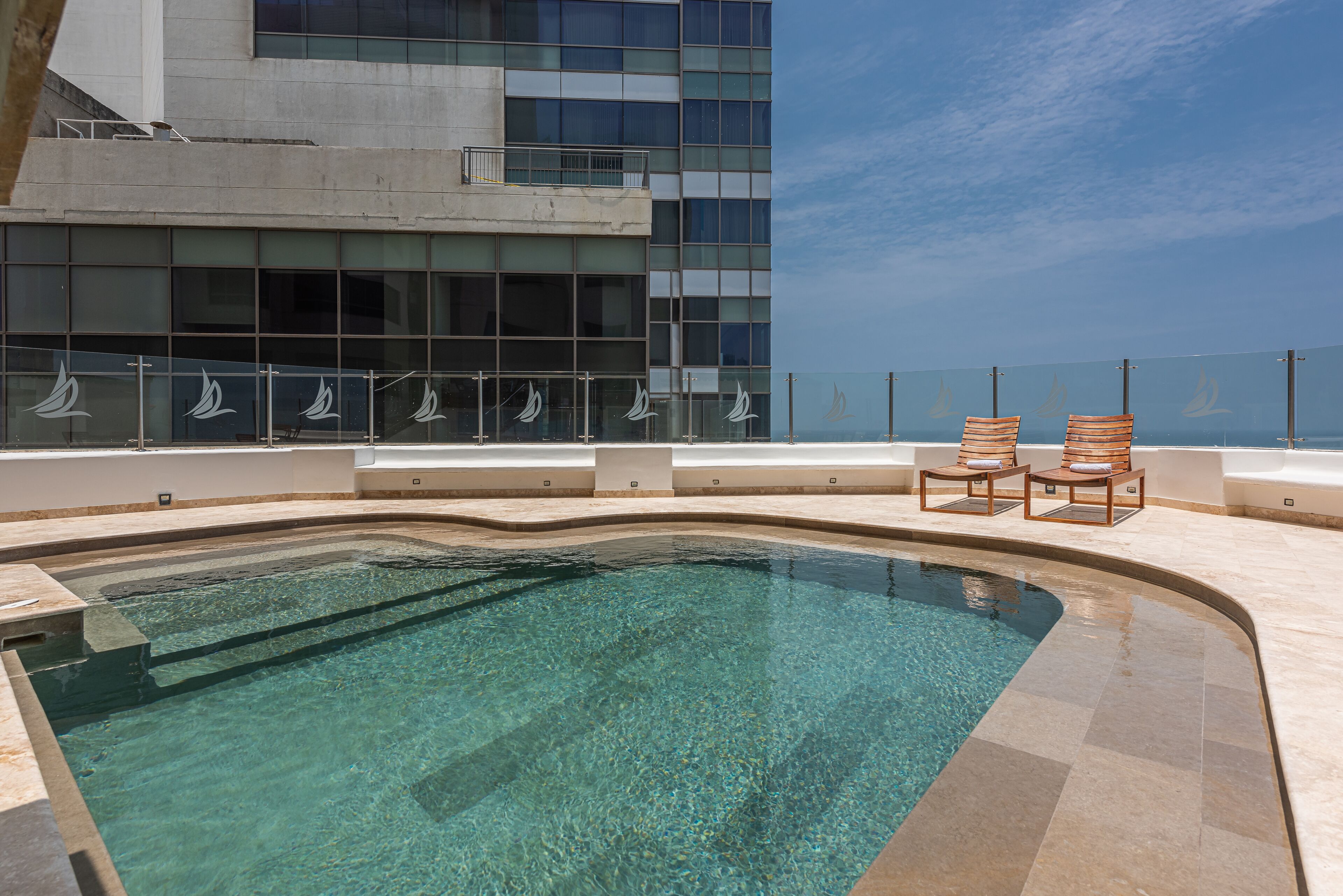 A swimming pool with clear water, two wooden chairs, and a modern building with large windows in the background.