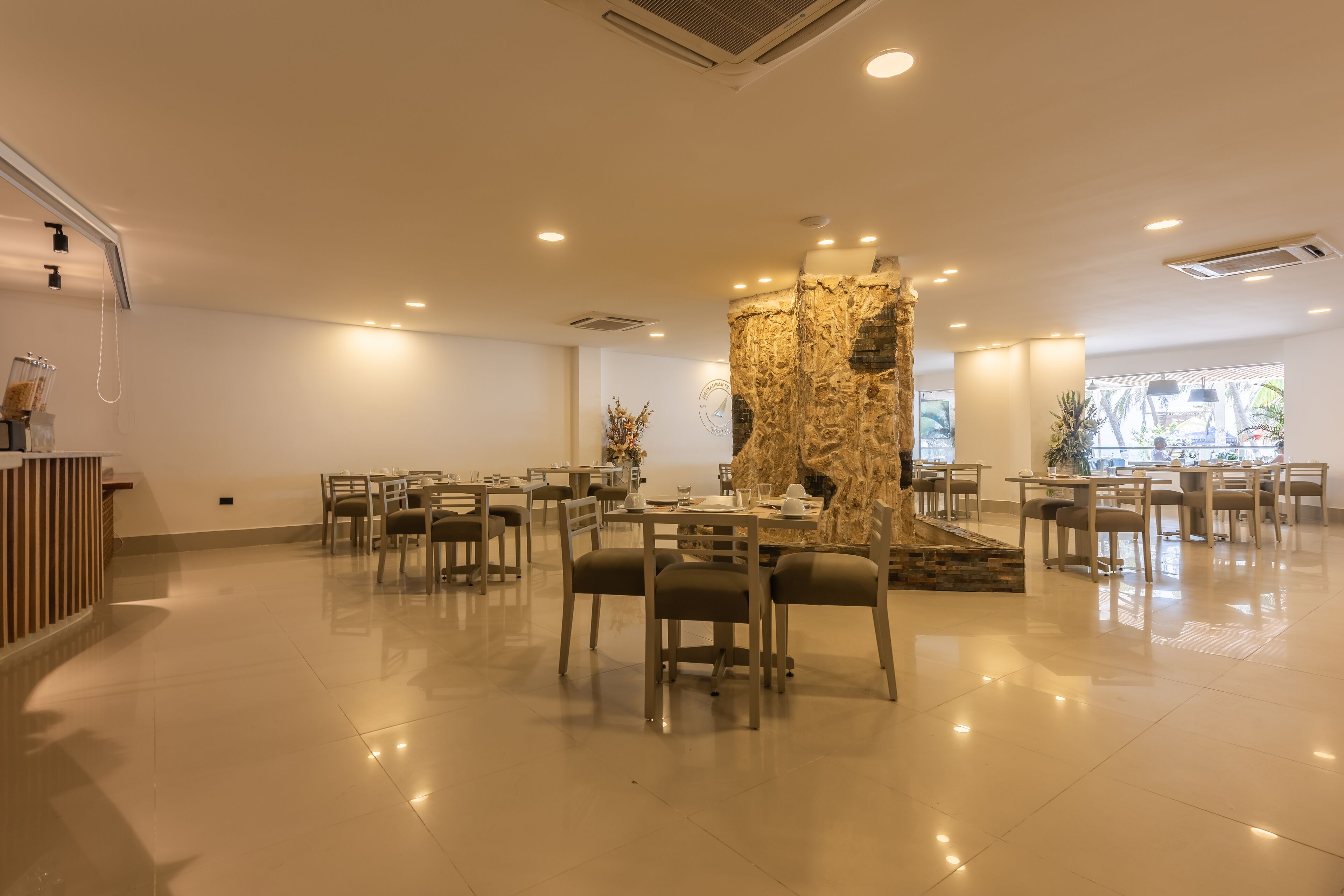 A spacious dining area with multiple tables and chairs, a central decorative column, and a reception desk.