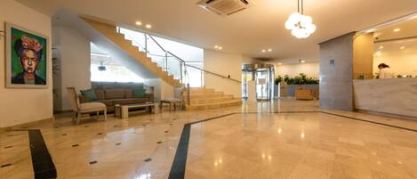 A spacious lobby with a marble floor, a staircase, and a reception desk.
