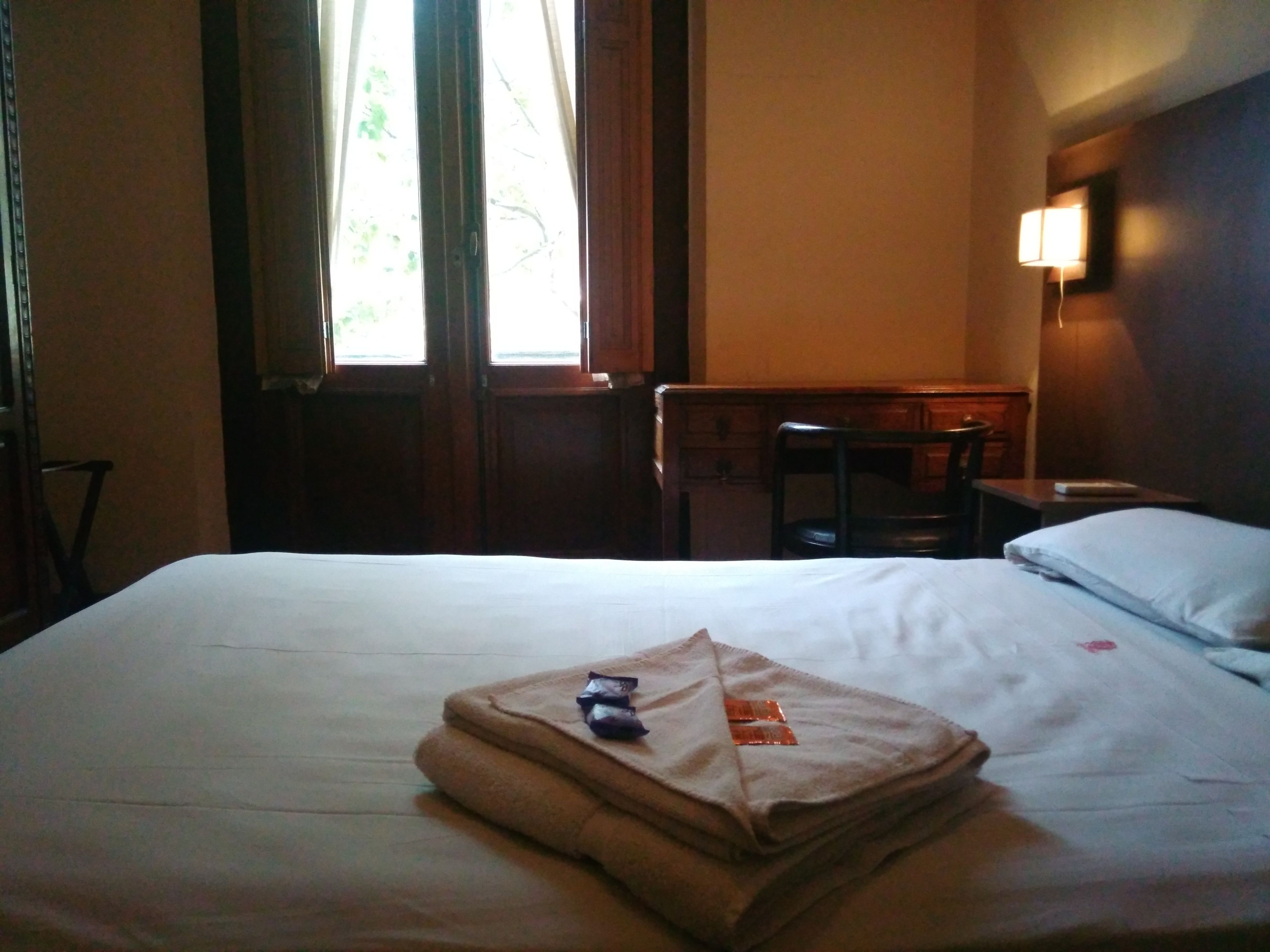 Une chambre d’hôtel avec un lit, une chaise, un bureau et une fenêtre avec des rideaux.