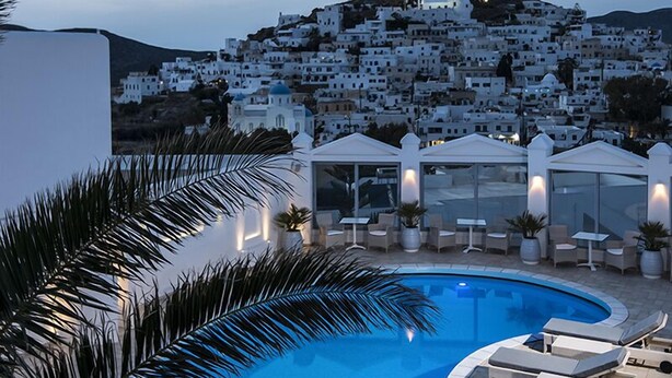 A pool area with lounge chairs and umbrellas, overlooking a hillside of white buildings. - Lofos Village Hotel (Ios)