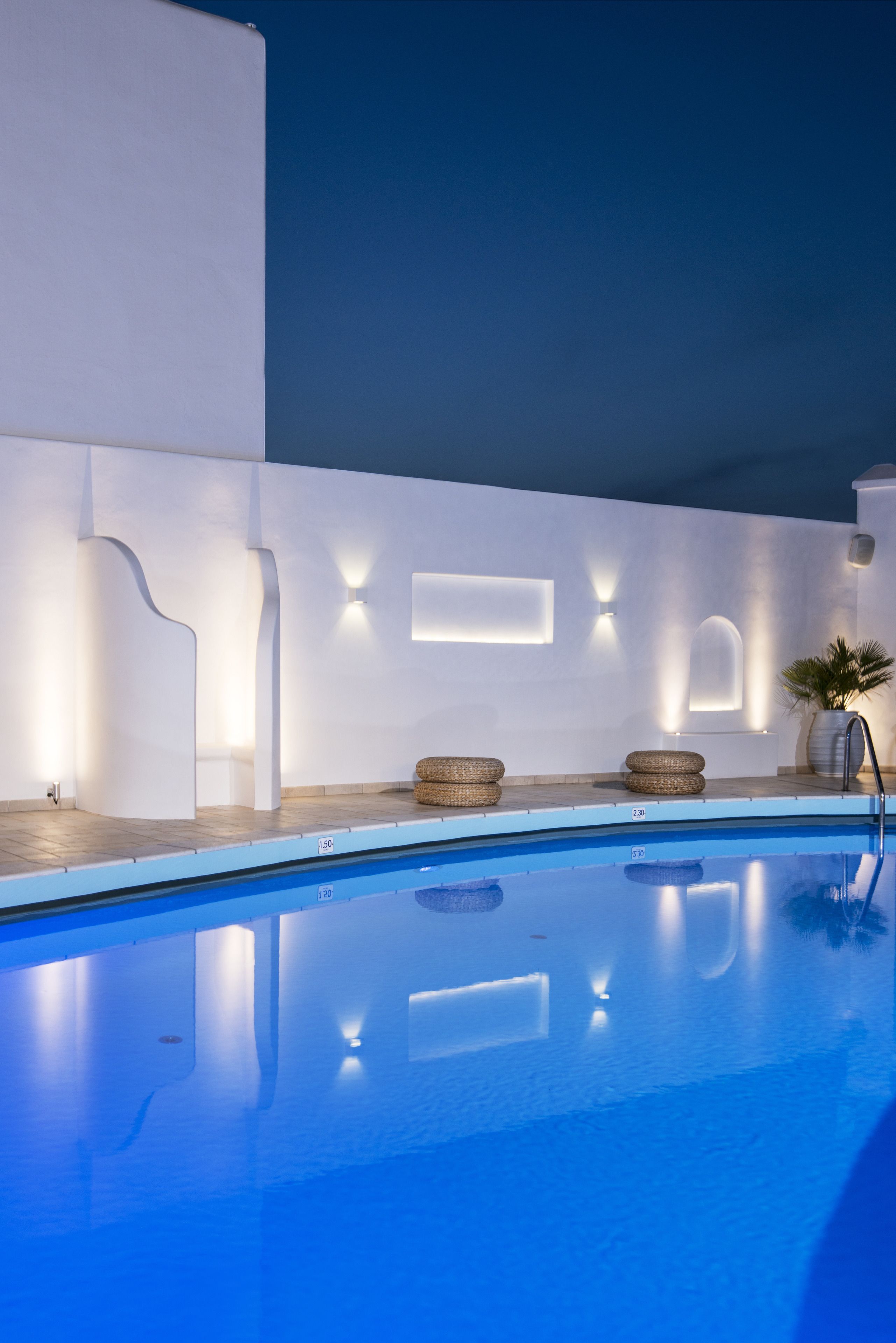 A swimming pool with a clear blue water surface, surrounded by white walls with built-in lighting fixtures.