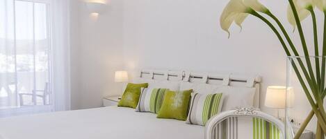 A neatly made bed with white bedding and green and white striped pillows, a white headboard, and a vase with white flowers on a bedside table.
