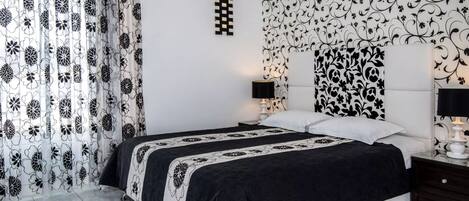 A bedroom with a bed, two bedside tables, a nightstand, a wall-mounted lamp, and a decorative wall panel.
