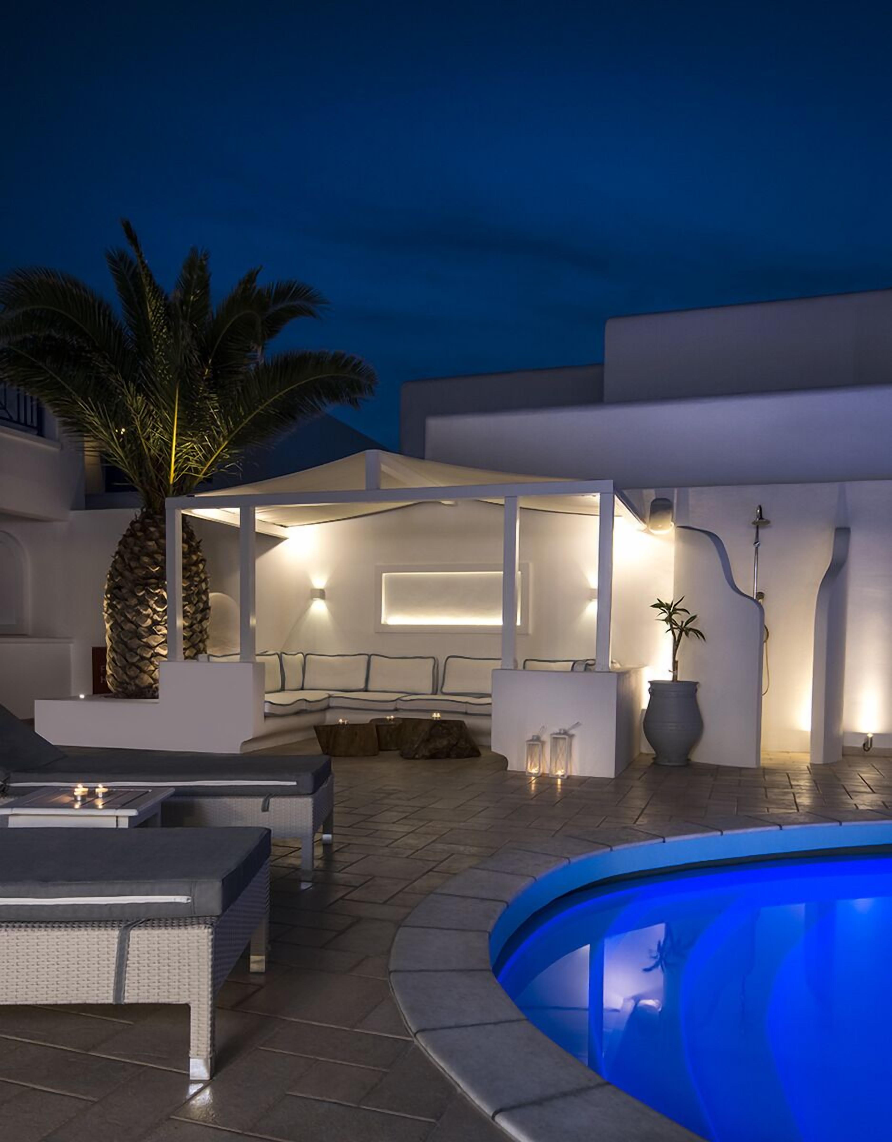 Un espace piscine extérieur moderne, doté d’une chaise longue, d’un palmier et d’un coin salon bien éclairé.
