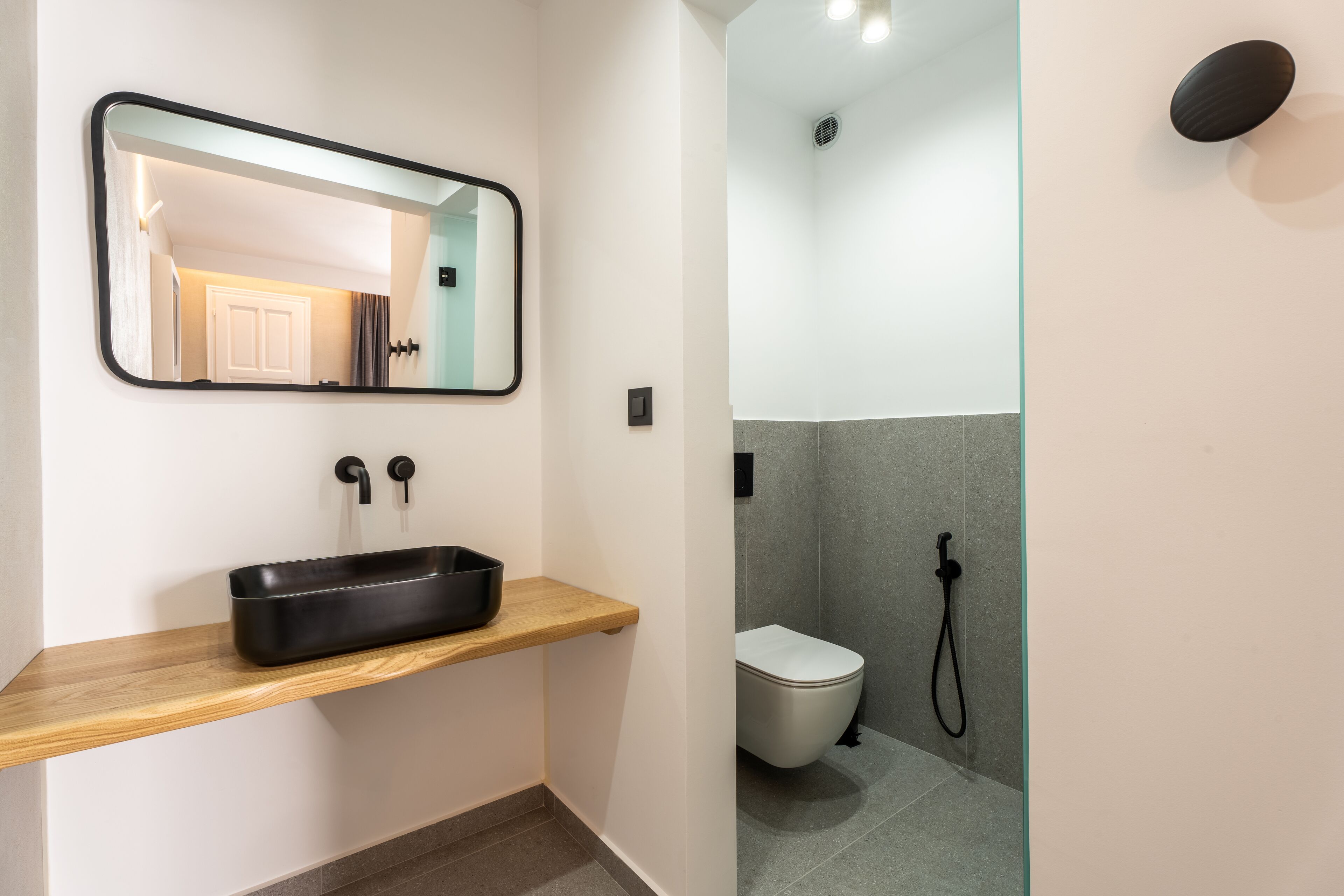 Une salle de bain avec une étagère en bois, un lavabo noir, des toilettes et une douche.