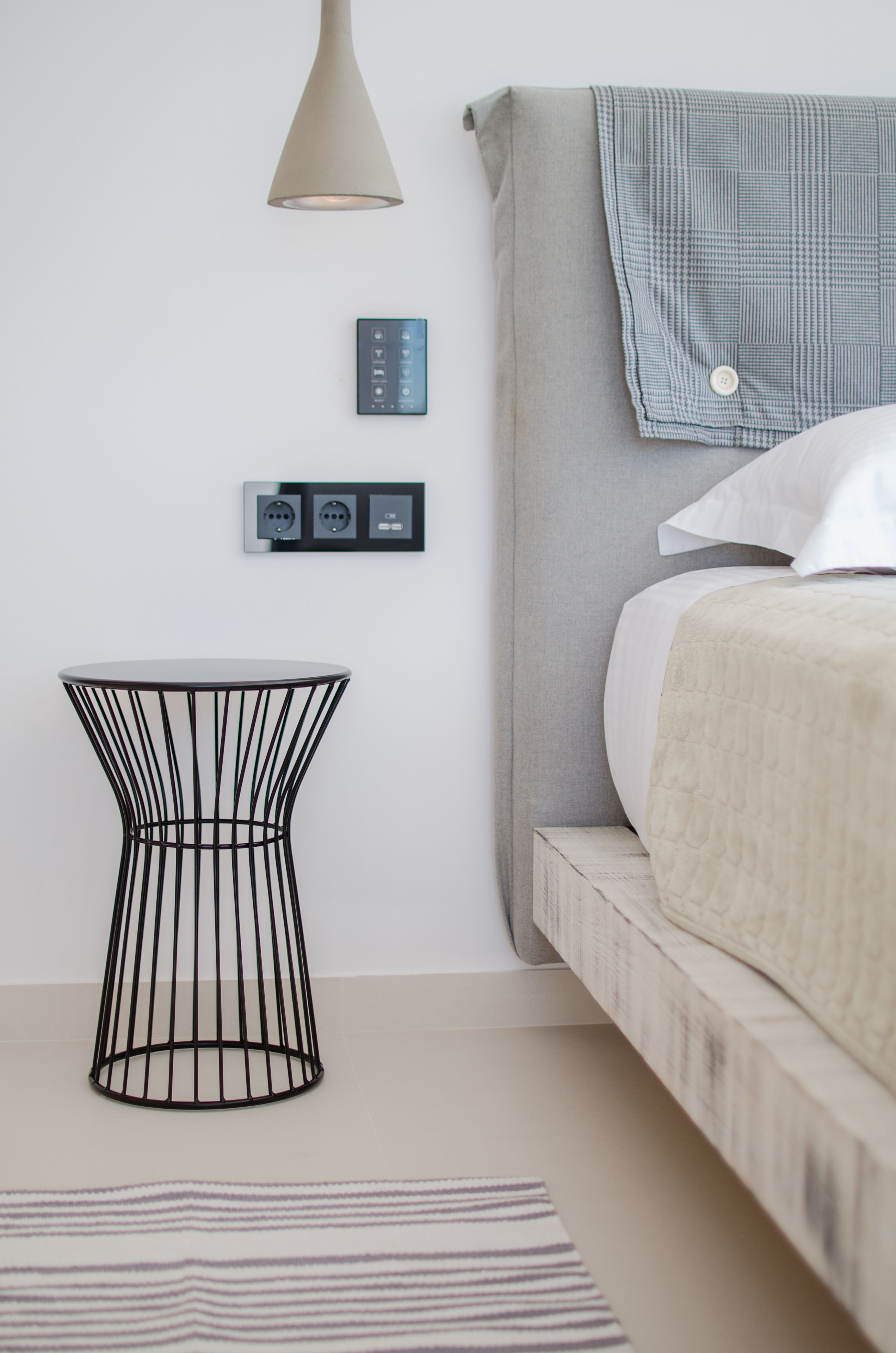 Ein modernes Schlafzimmer mit Bett, Nachttisch, Lampe und Wandsteuerelementen.