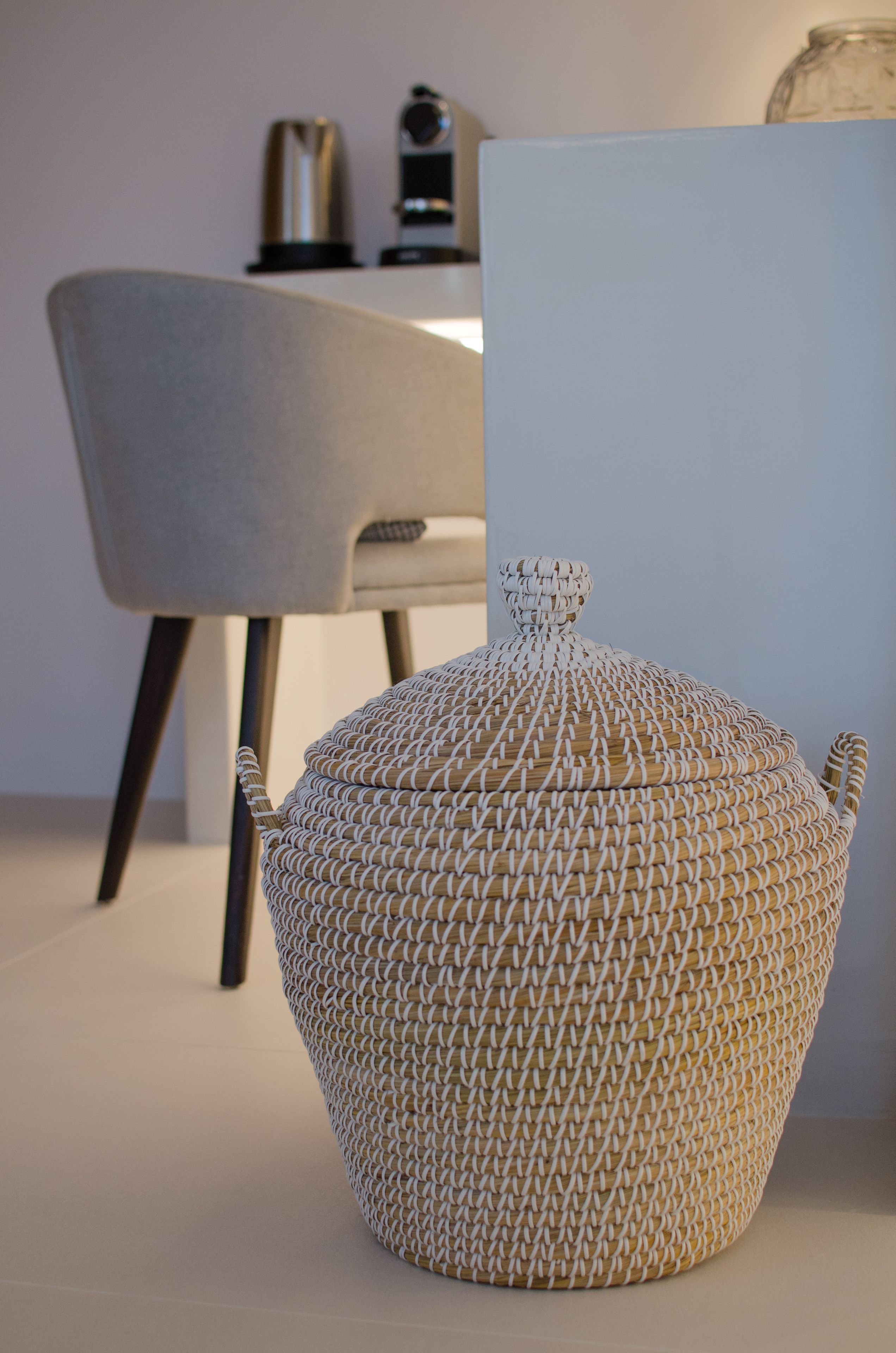 A woven basket with a lid, a chair, and a coffee machine in the background.