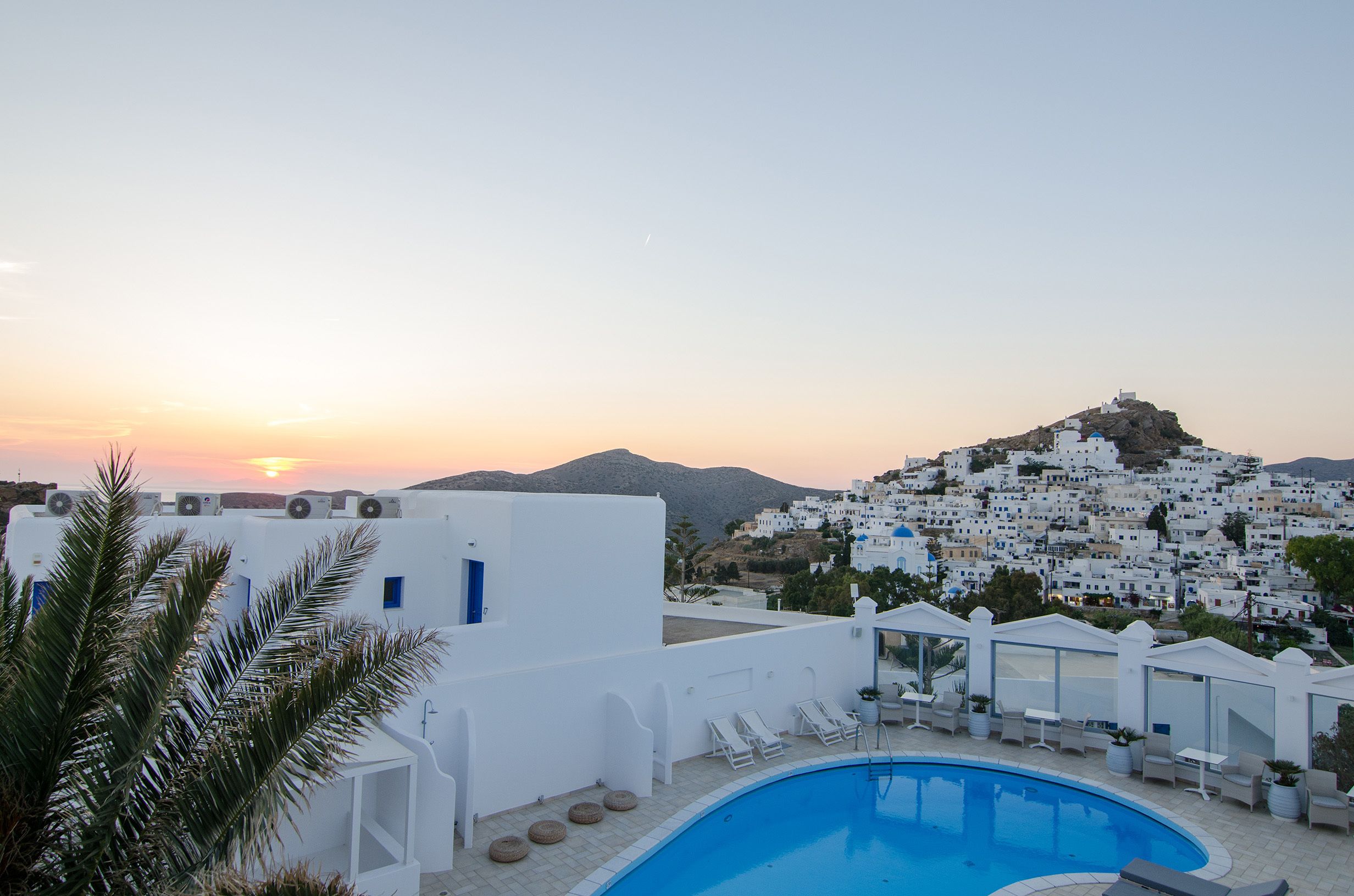 A rooftop pool area with white buildings and a mountain in the background.