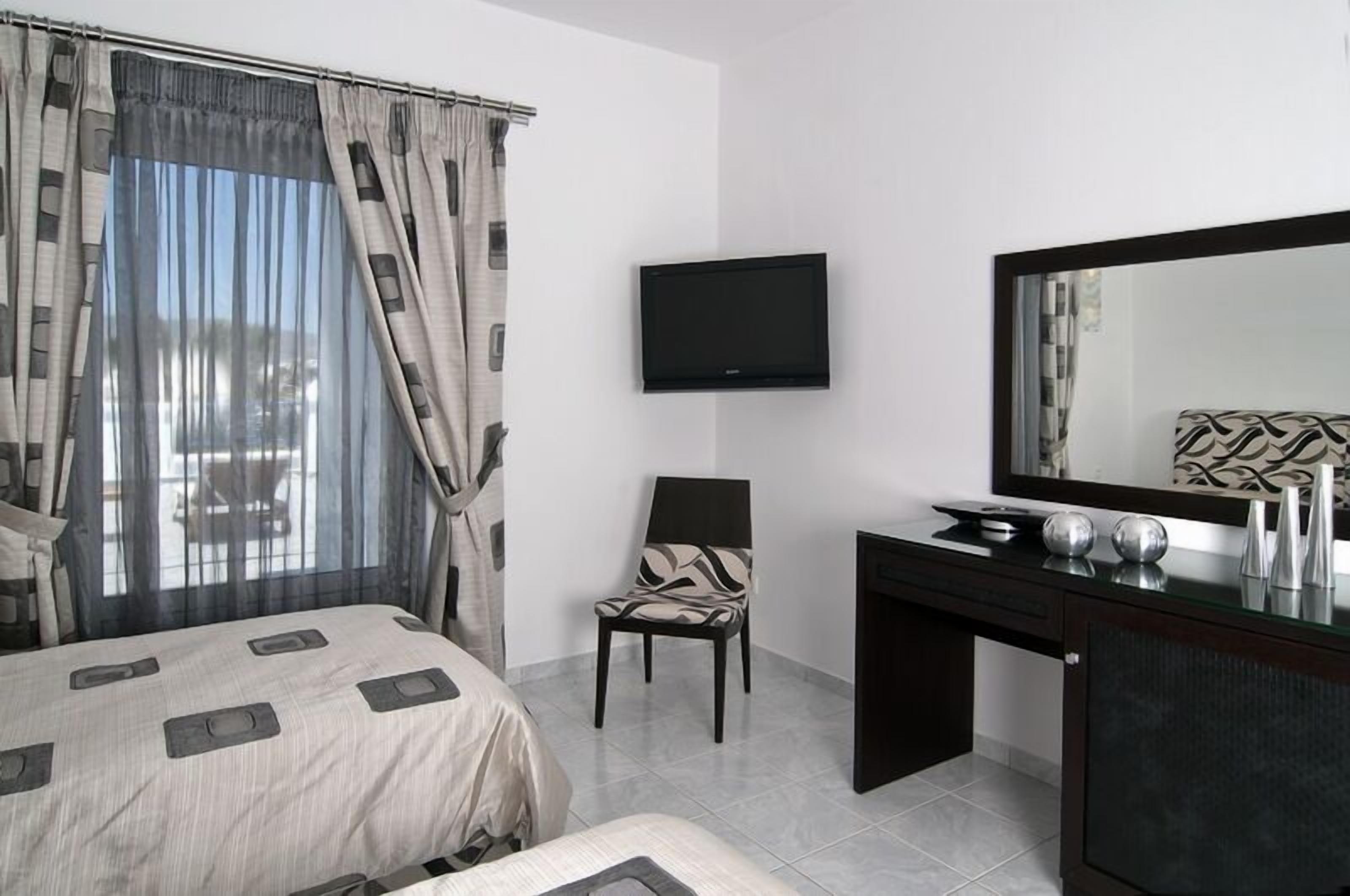 Habitación de hotel con cama, una silla, escritorio con espejo y televisor de pantalla plana montado en la pared.