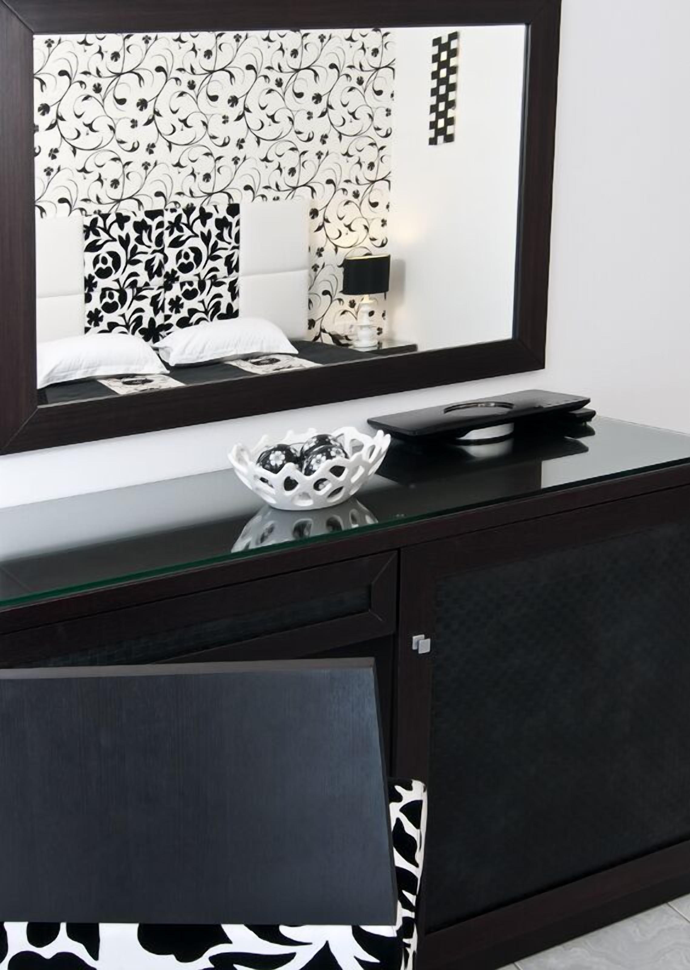 Une chambre à coucher moderne avec un grand miroir, une table de chevet avec une lampe et un vase décoratif posé sur la commode.