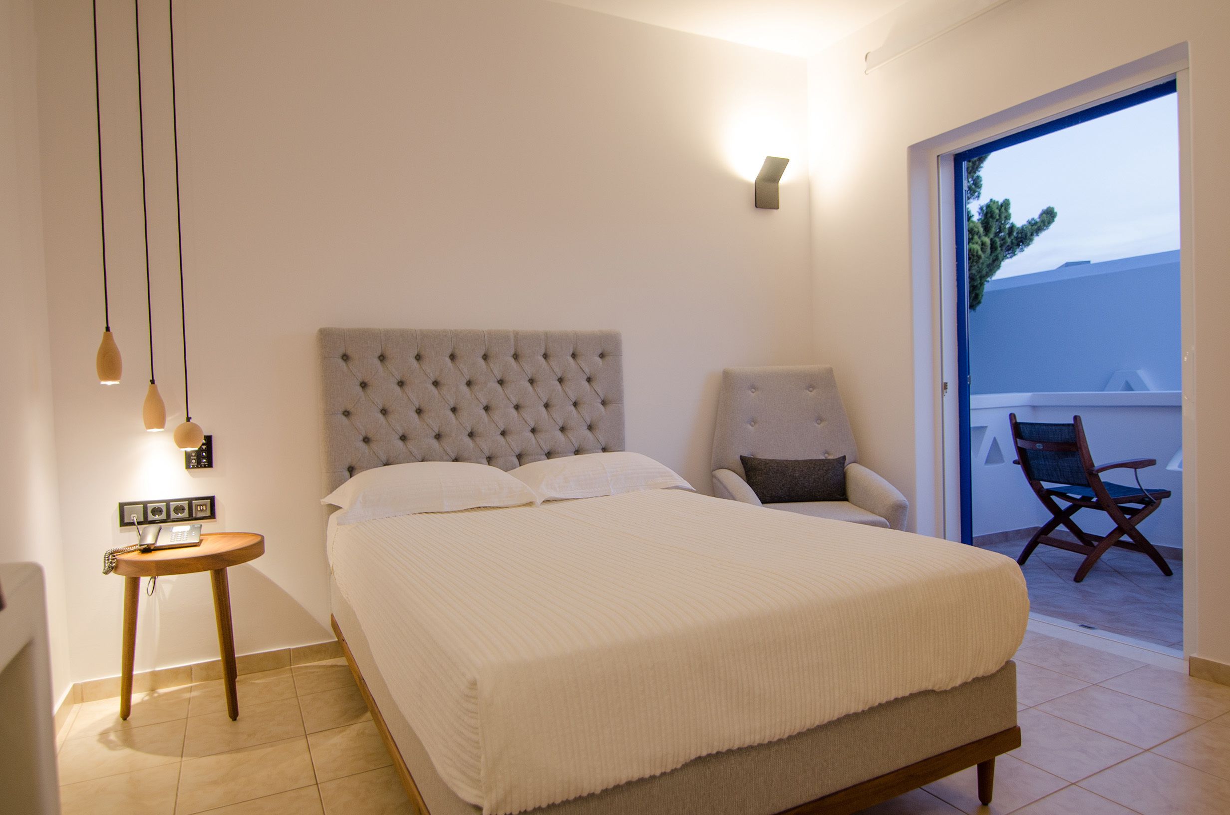 Quarto com uma cama grande, uma cadeira, uma mesinha com abajur e vista para o exterior.