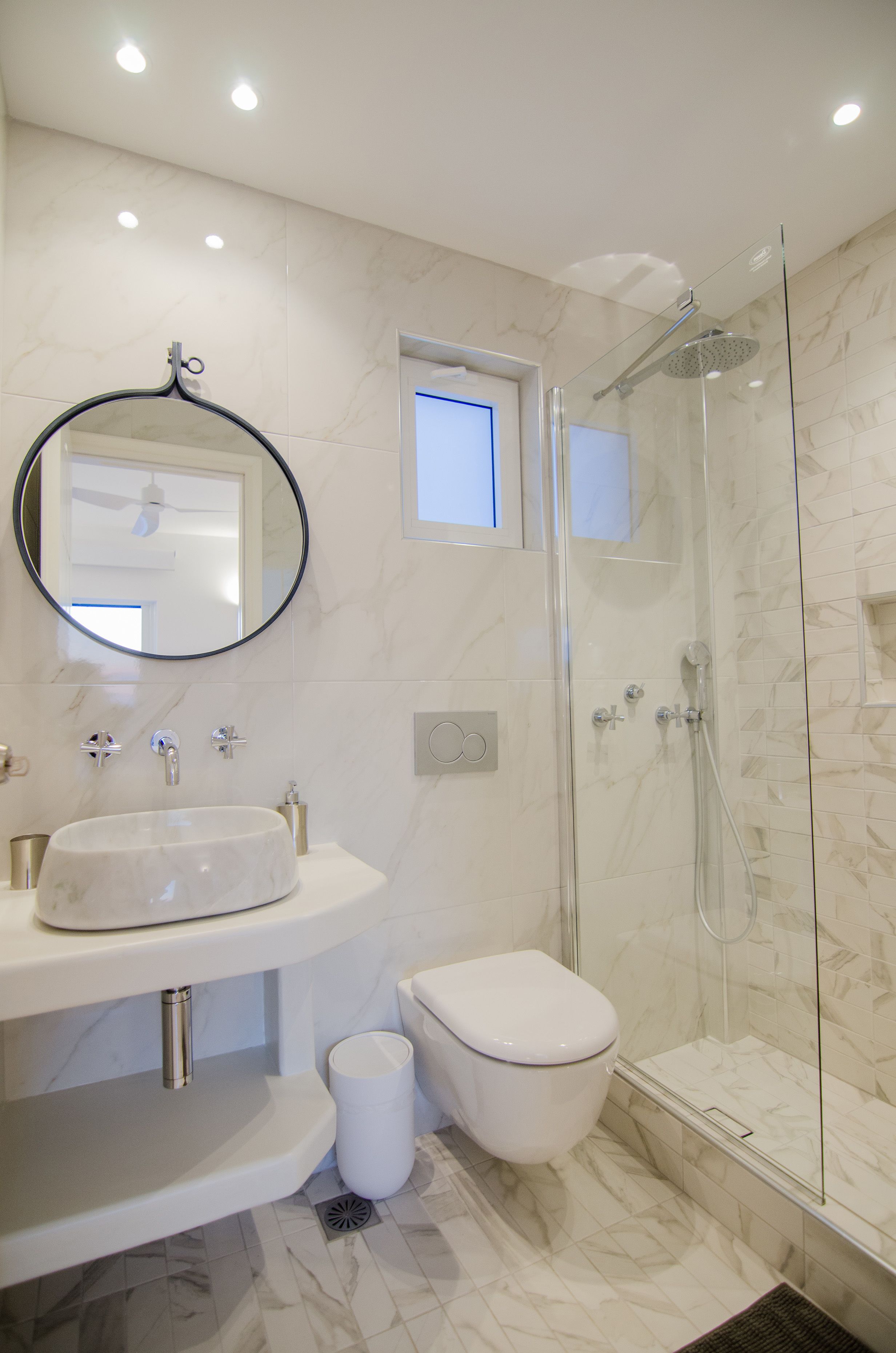 A modern bathroom with a marble sink, a toilet, and a glass-enclosed shower.