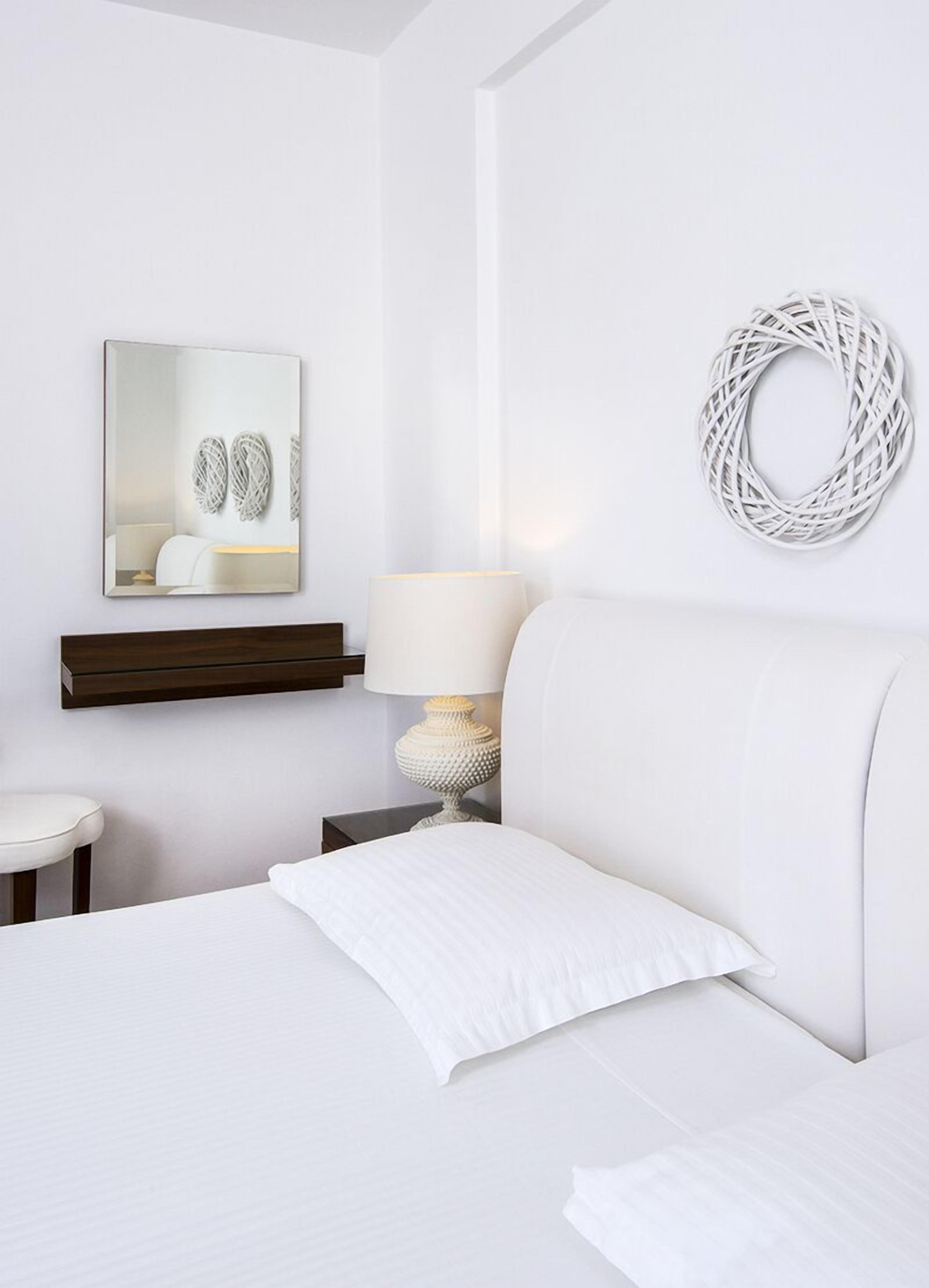 A hotel room with a bed, a bedside table, a lamp, a mirror, and a wall-mounted decorative item.