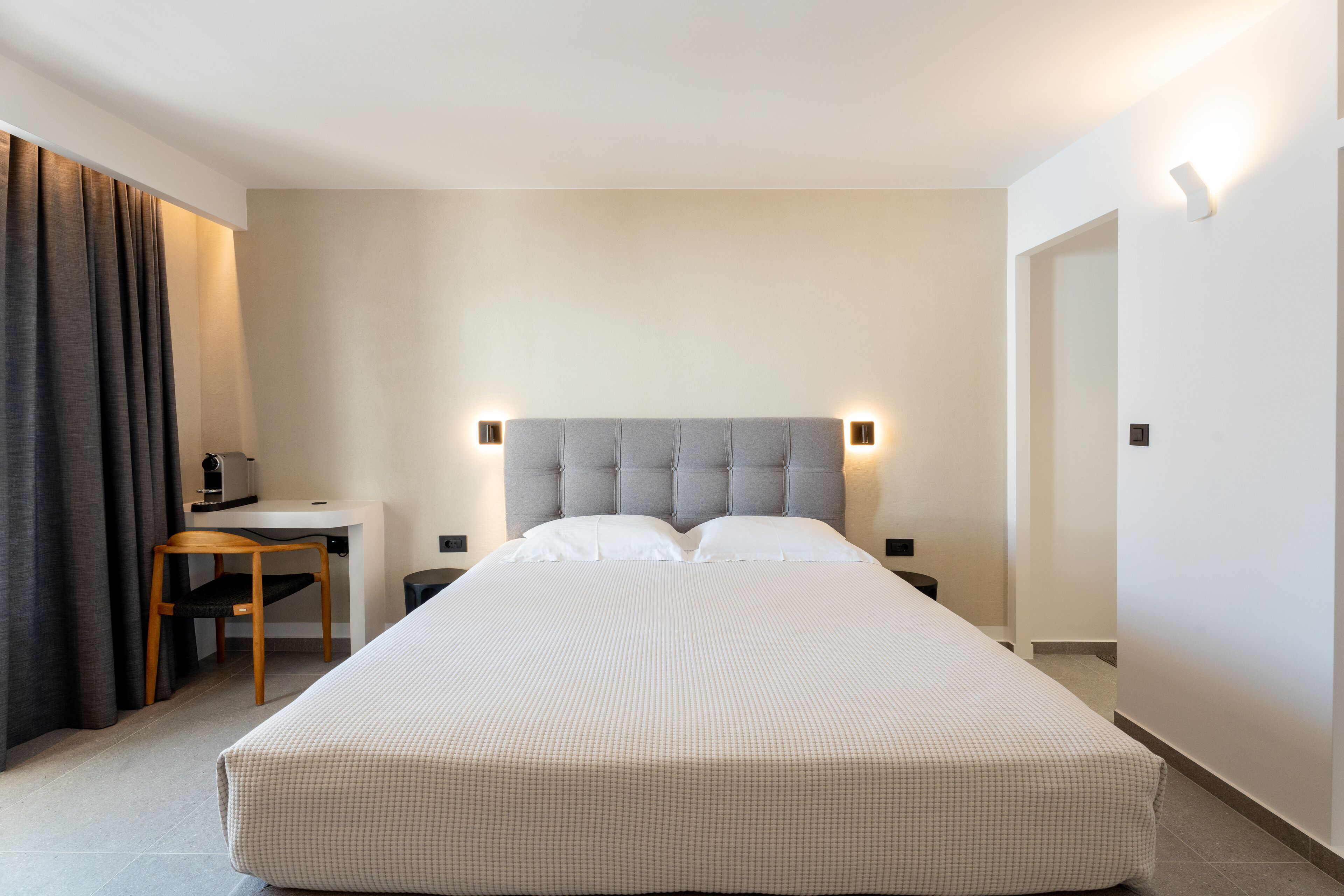A hotel room with a large bed, a desk, and a chair. There are two bedside tables and a lamp on each side of the bed.