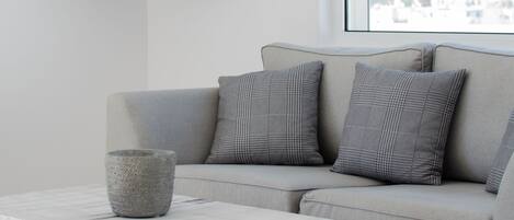 A modern living room with a grey sofa, a flat-screen TV mounted on the wall, and a marble coffee table.