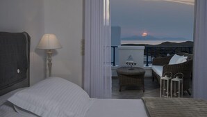 A bedroom with a bed, a bedside lamp, and a view of the balcony with a wicker chair, a small table, and two lanterns. - Lofos Village Hotel (Ios)