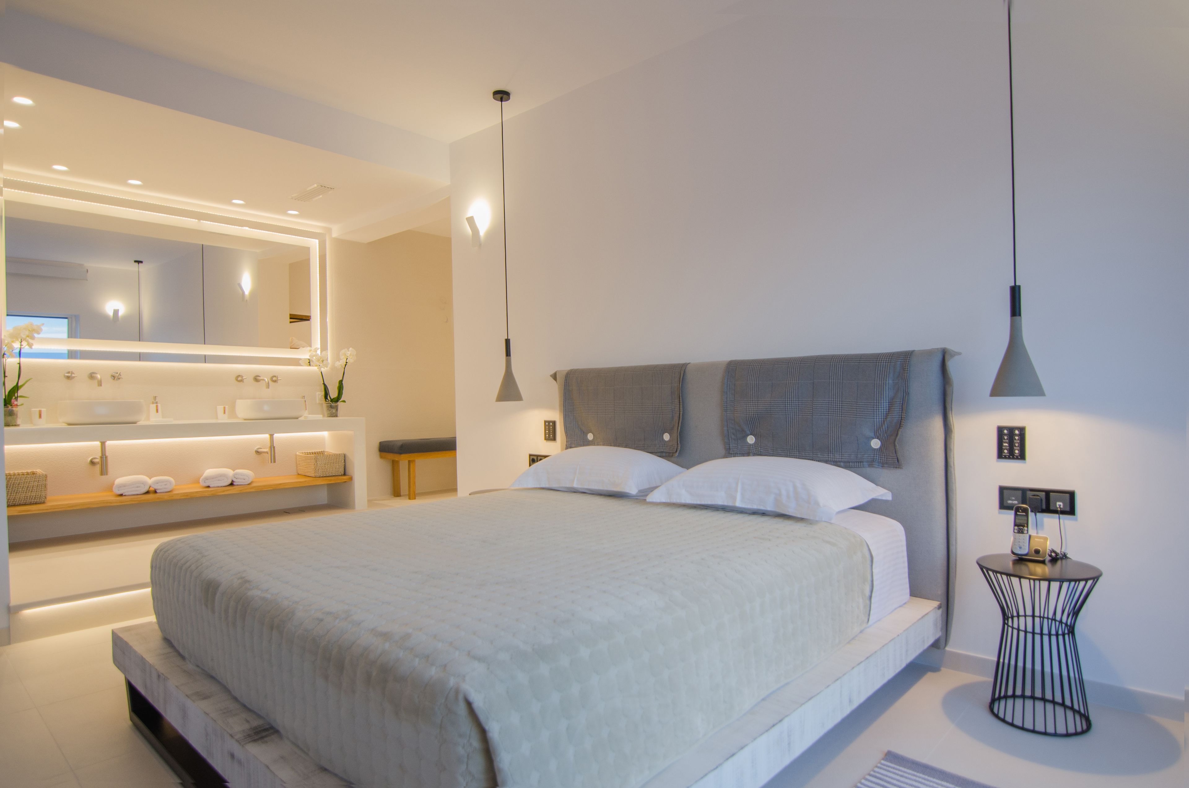A modern bedroom with a large bed, bedside tables, a vanity with a mirror, and a small side table with a lamp.
