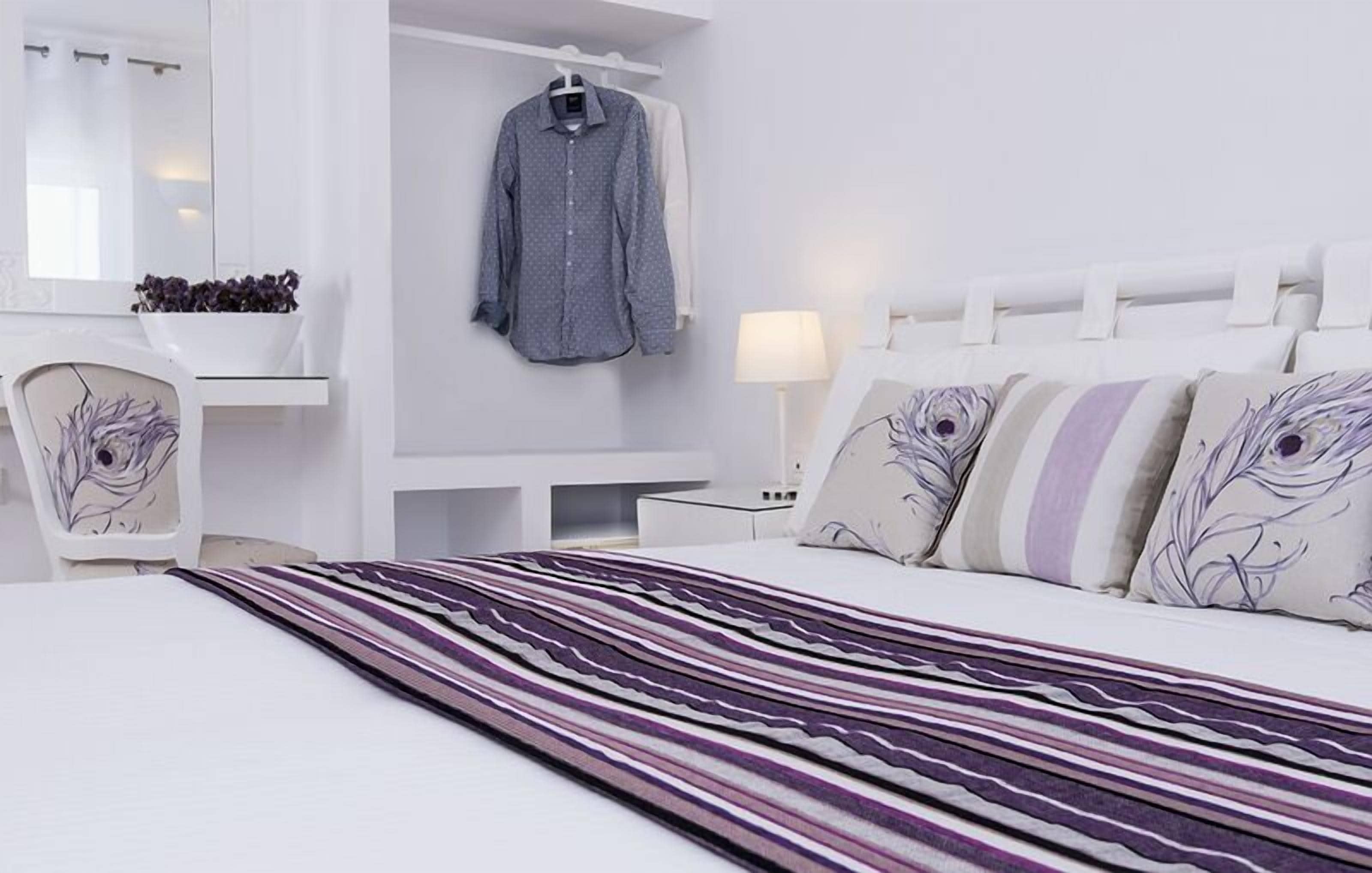 A modern hotel room with a large bed, a desk, a chair, and a hanging garment.