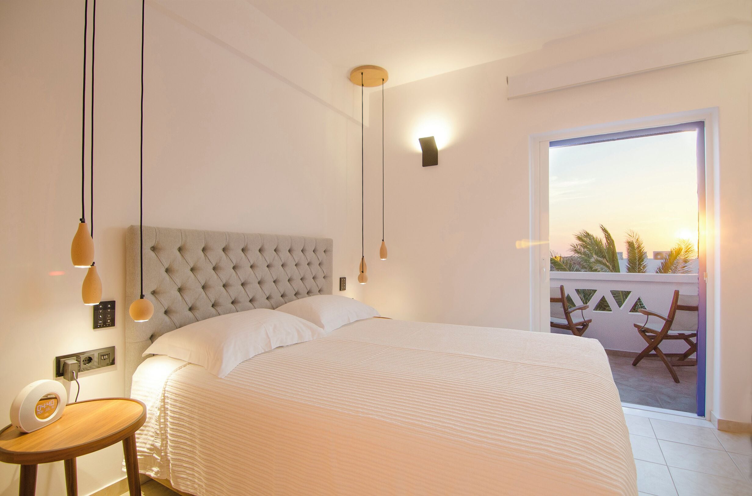 A bedroom with a large bed, bedside table, and a balcony with chairs.