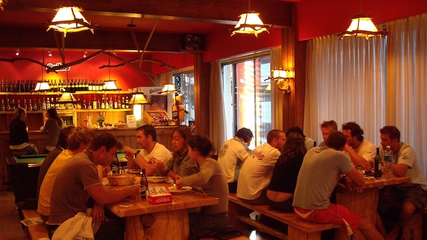 Eine Bar mit Holzbänken und -tischen, alkoholischen Getränken und einer roten Wand mit einem Schild.