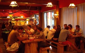 Een bar met houten banken en tafels, drankflessen en een rode muur met een bord.