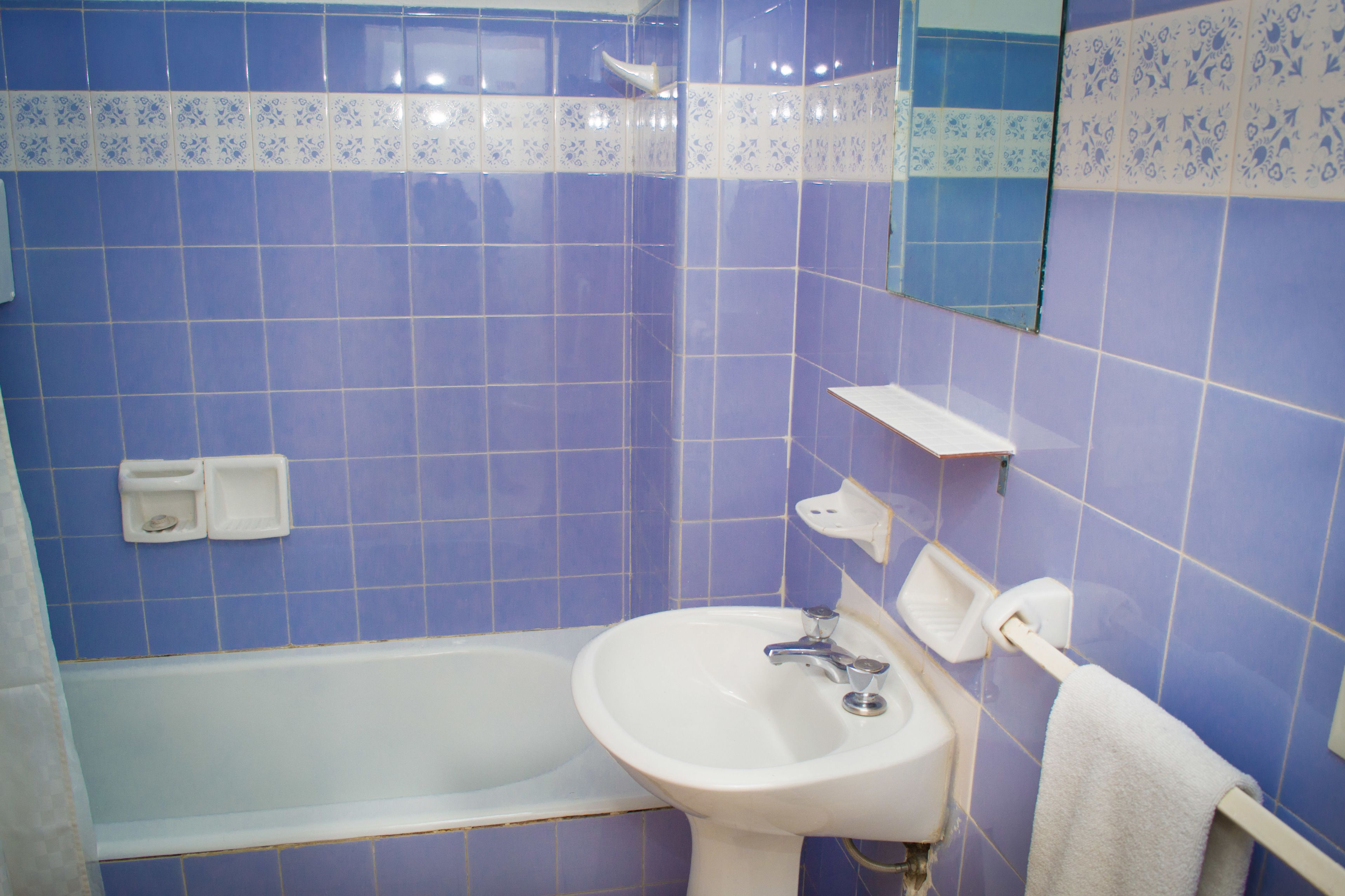A bathroom with blue tiles, a white sink, a white bathtub, and a towel rack.