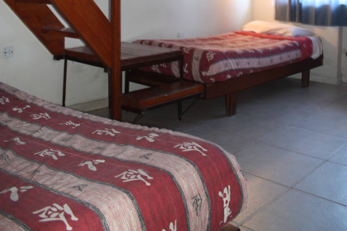 A room with two beds, wooden beams on the ceiling, and wall-mounted lights.
