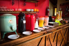 A breakfast bar with various food and drink containers, plates, and a coffee maker. - Hostel Inn Calafate (El Calafate)