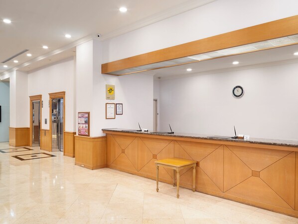 A reception area with a wooden reception desk, a clock on the wall, and a tiled floor.