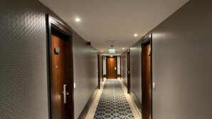 A long, narrow hallway with patterned carpet, wooden doors, and recessed lighting.