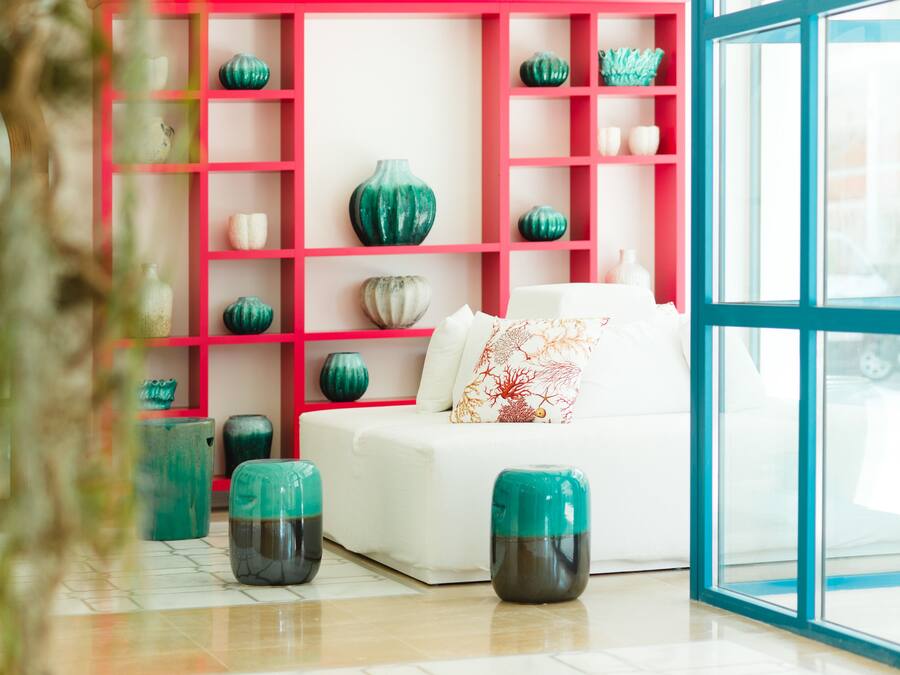 A modern living room with a white sofa, teal and green decorative vases, and a pink shelving unit.