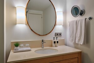 Un baño con un espejo redondo, dos luces empotradas, un lavamanos y un perchero para toallas.