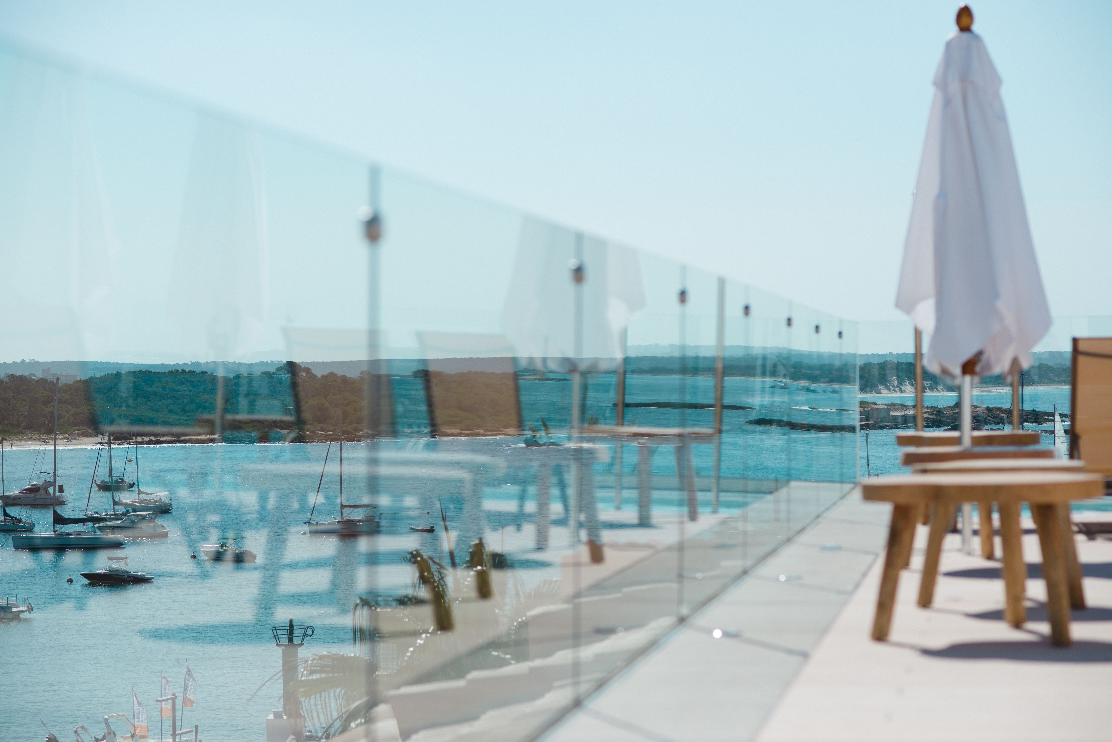Een glazen terras met houten stoelen en een witte parasol, met uitzicht op een jachthaven met boten.
